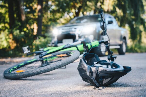 Close-up of a bicycling helmet fallen on the asphalt next to a bicycle after car accident on the road. Kentucky accident lawyers Saladino & Schaaf.