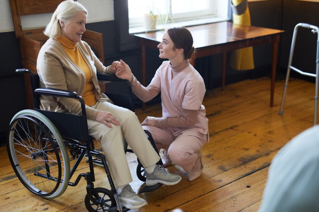 Elderly woman in nursing home sitting in wheel chair being counseled by nurse.