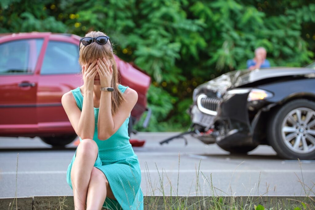 Car Accident with stressed woman sitting on street side.
