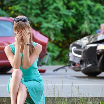 Car Accident with stressed woman sitting on street side.