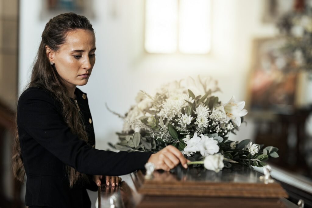 Funeral, sad and woman with flower on coffin after loss of a loved one, family or friend. Grief, de