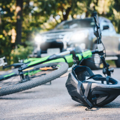 Close-up of a bicycling helmet fallen on the asphalt next to a bicycle after car accident on the road. Kentucky accident lawyers Saladino & Schaaf.
